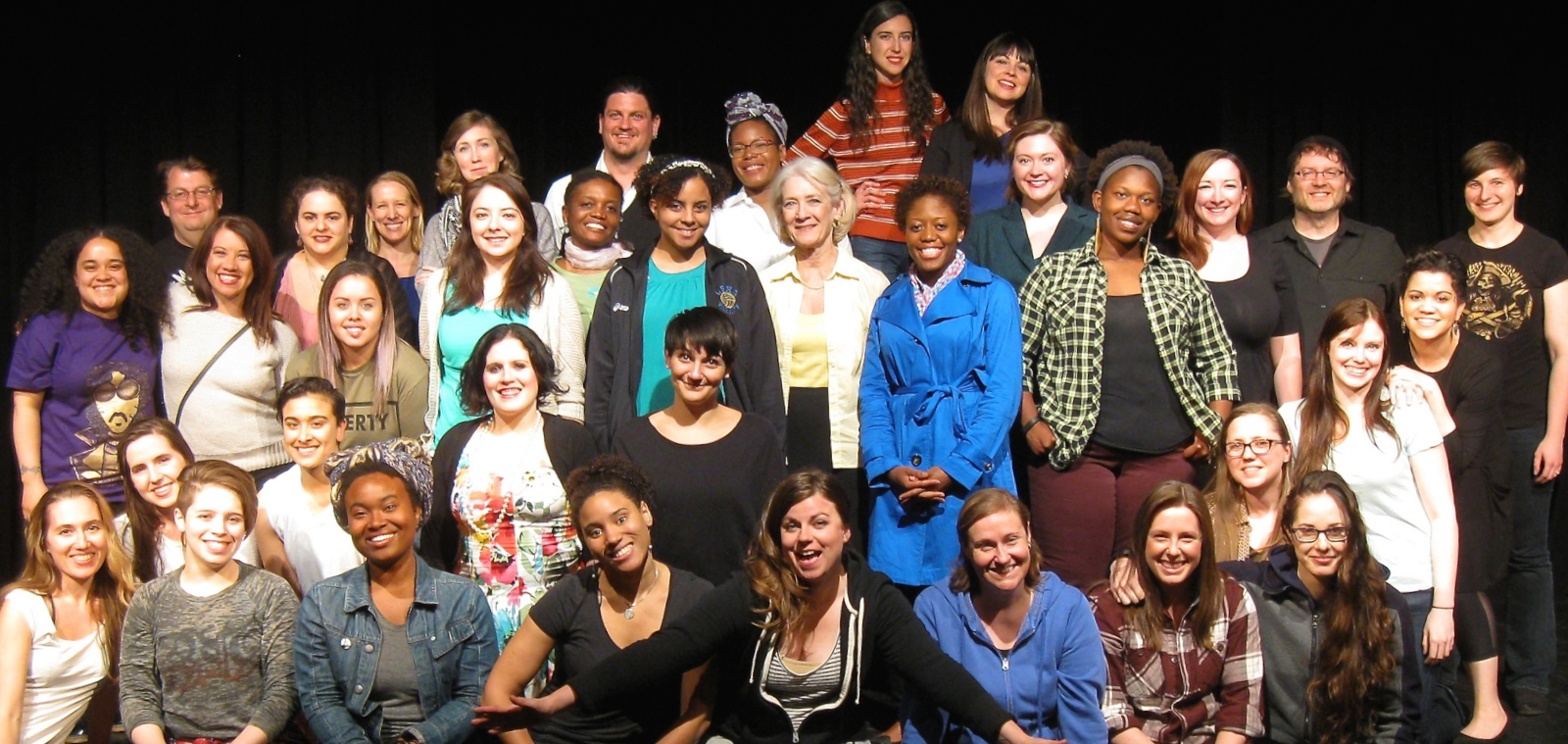 A group photo of 36 artists on a stage, smiling at the camera